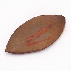 Puede incluir: Un plato de cerámica marrón con forma de hoja y un diseño pintado en rojo anaranjado. El plato tiene una superficie texturizada y está sobre un fondo blanco. El plato mide aproximadamente 25 cm de largo.