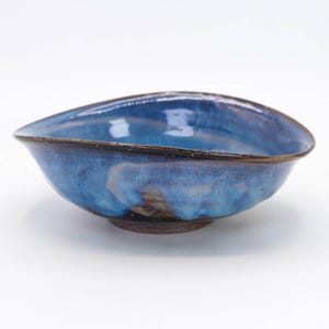 May include: A blue ceramic bowl with a dark brown rim and a slightly irregular shape. The bowl has a mottled blue glaze with hints of purple and white.