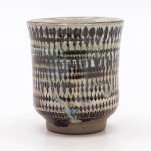 May include: A cylindrical ceramic cup featuring a repeating vertical pattern of dark brown and cream-colored markings. The exterior surface displays a textured, layered glaze with subtle hints of blue, while the base remains an unglazed, matte brown.