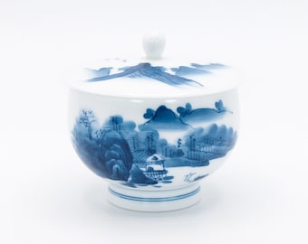 May include: A white porcelain bowl with a blue and white landscape design. The bowl has a lid with a matching design. The bowl is approximately 4 inches in diameter.