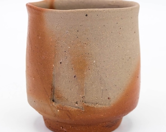 Puede incluir: Una taza de cerámica marrón y beige con una superficie texturizada. La taza tiene una forma redondeada y un borde ligeramente acampanado.