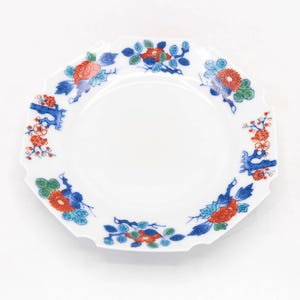 May include: White octagonal plate with a floral design. The plate features red and orange flowers, blue leaves, and branches. The flowers and leaves are arranged around the rim of the plate.