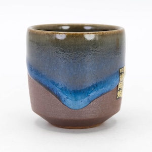 May include: A small, brown and blue ceramic teacup with a textured glaze. The cup has a rounded bottom and a slightly flared rim. The text "福田陶苑" is printed on the side of the cup.