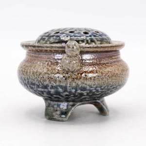Side view of vintage Mashiko ware koro, three legged incense burner with flowing salt glaze and earthy tones