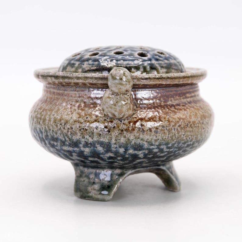 Side view of vintage Mashiko ware koro, three legged incense burner with flowing salt glaze and earthy tones