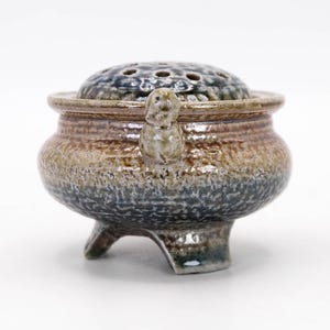 Side view of vintage Mashiko ware koro, three legged incense burner with flowing salt glaze and earthy tones