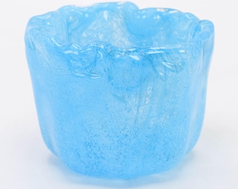 Op de afbeelding: Een lichtblauwe glazen votiefkaarsenhouder met een textuuroppervlak en een golvende rand. De kleine, ronde container is gemaakt van doorschijnend glas. De kaarsenhouder is ongeveer 7.6 cm hoog.
