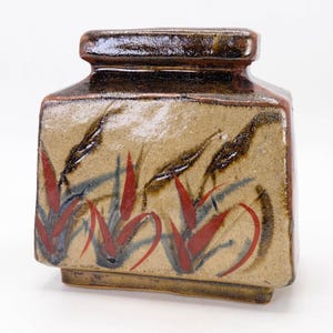 May include: A square ceramic vase with a brown glaze and a design of red and black stylized leaves. The vase has a wide mouth and a flat base.