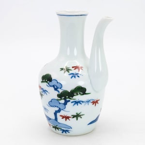 May include: White ceramic sake bottle with a blue, green and red painted design of a pine tree and maple leaves.