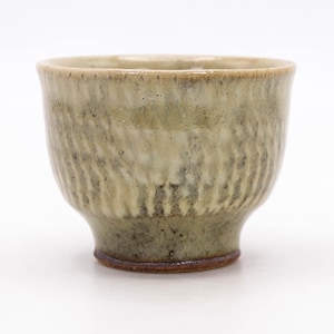 Puede incluir: Una taza de té de cerámica hecha a mano con un exterior texturizado y acanalado. La taza tiene una combinación de colores verde claro y marrón, con una base marrón más oscura. La taza está diseñada con una forma redondeada y un borde ligeramente ensanchado.