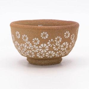 May include: A small, round, ceramic bowl with a textured, light brown exterior. The bowl is decorated with a repeating pattern of white, stylized flower shapes. The bowl has a slightly flared rim and a small, raised base.