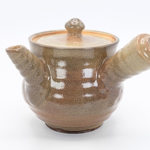 Może przedstawiać: Brązowy ceramiczny czajnik z pękniętą glazurą i dzi&oacute;bkiem z boku. Czajnik ma pokrywkę z małym uchwytem na g&oacute;rze.