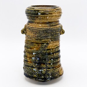 May include: A ceramic vase with a textured, striped design in shades of brown and green. The vase has a wide mouth and a rounded base.