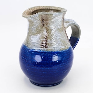 May include: A blue and white ceramic pitcher with a textured glaze. The pitcher has a rounded body and a handle.