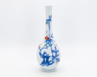 May include: A white ceramic vase with a blue and red floral design. The vase has a narrow neck and a round body. The floral design features bamboo stalks, flowers, and leaves.