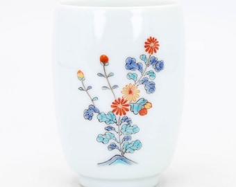 May include: White ceramic cup with a floral design featuring blue, orange, and yellow flowers and green leaves. The flowers are painted in a traditional Japanese style.