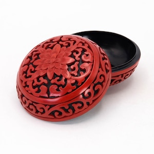 May include: A red and black round trinket box with intricate floral carvings. The lid is open and the inside is black.