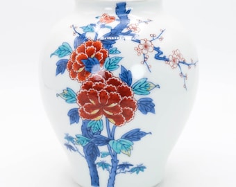 May include: A white ceramic vase with a floral design. The vase has a round body and a narrow neck. The floral design features red, blue, and green flowers and leaves.