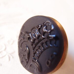 Pu&ograve; includere: Un bottone nero con un bordo dorato e un design decorativo. Il design &egrave; un motivo floreale stilizzato.