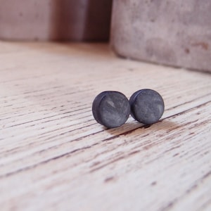 Peut inclure: Une paire de petites boucles d'oreilles rondes noires. Les boucles d'oreilles ont une surface marbrée et texturée.
