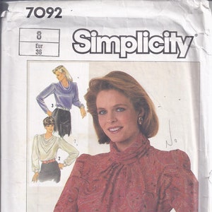 May include: Simplicity sewing pattern envelope featuring a woman in a paisley print blouse and black skirt. The envelope shows a pattern for a blouse with a high collar and long sleeves. The number 7092 is visible at the top.