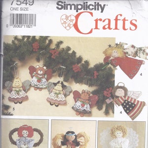 May include: A Simplicity Crafts pattern showcasing angel-themed decorations. The image displays hanging ornaments with animal faces and patriotic designs, alongside tree toppers. The toppers include a doll with a wreath and a Native American-inspired angel.