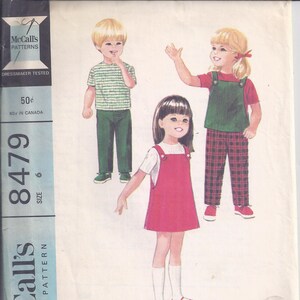 May include: Vintage McCall's pattern 8479 featuring illustrations of children's clothing. The pattern includes a child's jumper or jerkin, blouse, and pants. The cover displays a red jumper, green overalls, and a striped shirt.