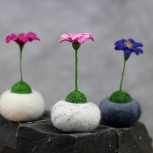 Puede incluir: Tres arreglos florales de fieltro en macetas blancas, grises y blancas. Las flores son rosas, azules y moradas.
