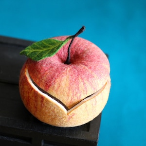 Puede incluir: Una manzana de fieltro de color rojo y amarillo, dividida para revelar un interior blanco. La manzana está sobre una superficie negra.