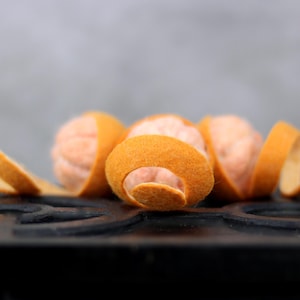 Puede incluir: Primer plano de cáscaras de naranja enroscadas alrededor de una fruta cítrica rosa. Las cáscaras son de color naranja claro y la fruta es de color rosa pálido. La fruta y las cáscaras están sobre una superficie negra.