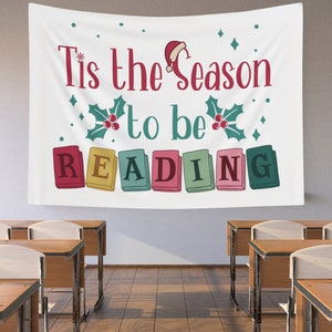 May include: White fabric wall hanging with the text "Tis the Season to be READING" in red and green. The design includes a Santa hat, holly, and colorful book illustrations. The banner is displayed in a classroom setting.