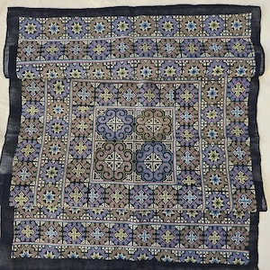 Könnte beinhalten: Ein schwarzes Stoffquadrat mit einem bunten Stickmuster. Das Muster zeigt ein zentrales Quadrat mit komplizierten Mustern in Grün-, Blau- und Violetttönen. Der umgebende Bereich ist mit kleineren Quadraten in verschiedenen Farben gefüllt, darunter Rosa, Gelb und Weiß.
