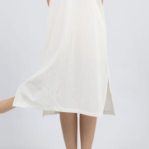 May include: A white sleeveless maxi dress with a side slit. The dress is made of a lightweight fabric and has a relaxed fit.