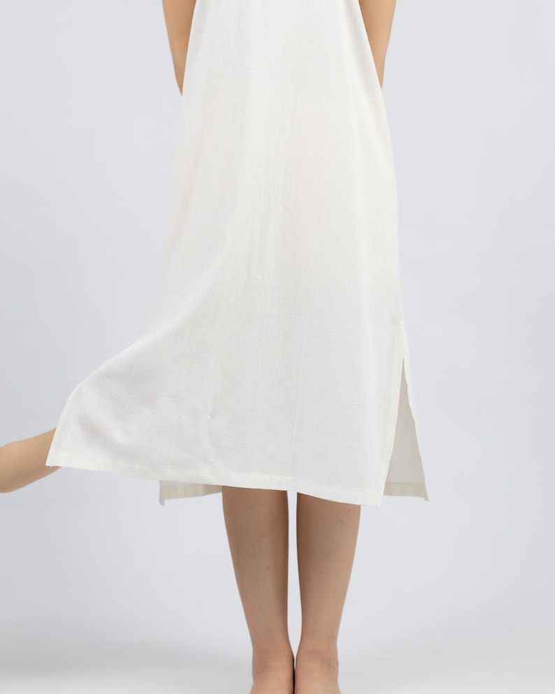 May include: A white sleeveless maxi dress with a side slit. The dress is made of a lightweight fabric and has a relaxed fit.