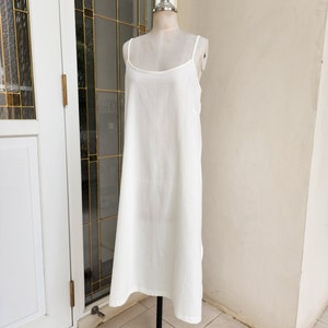 May include: A white sleeveless maxi dress with a simple, straight silhouette. The dress is made of a lightweight, flowy fabric and has a relaxed fit.