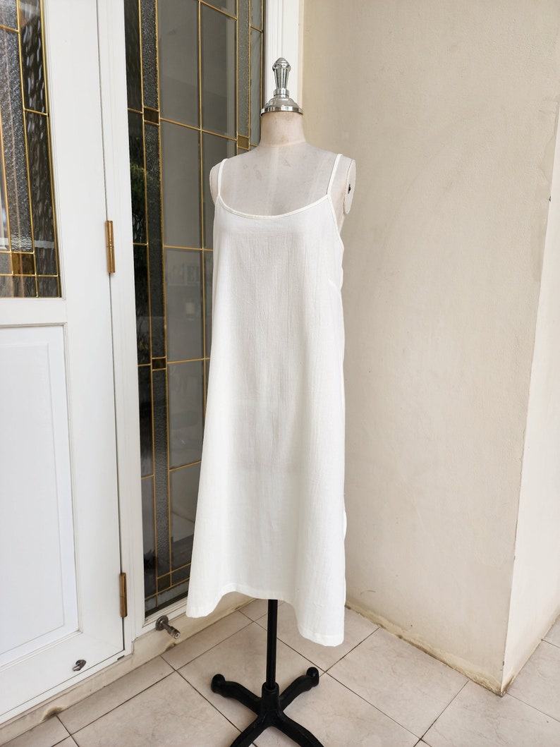 May include: A white sleeveless maxi dress with a simple, straight silhouette. The dress is made of a lightweight, flowy fabric and has a relaxed fit.