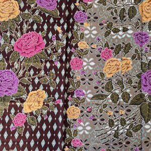 Op de afbeelding: Een textiel met een bloemenpatroon met roze, paarse en gele rozen. De rozen staan tegen een donkerbruine achtergrond met een ruitpatroon aan de ene kant en een grijs bloemmotief aan de andere kant. Groene bladeren en stelen maken het ontwerp compleet.