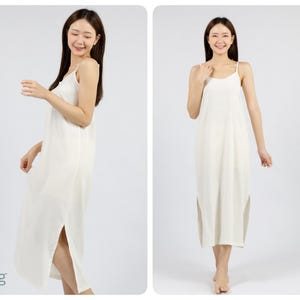 May include: A white sleeveless maxi dress with a side slit. The dress is made of a soft, flowing fabric and has a simple, elegant design. The model is wearing the dress and standing in front of a white background. The word "Long" is written in blue text at the bottom left of the image.