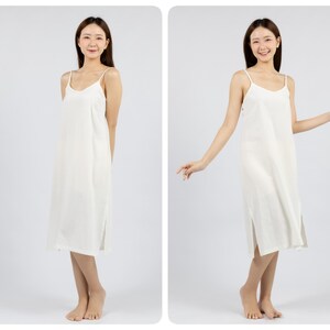 May include: A white midi slip dress with thin straps. The dress has a straight silhouette and a slightly flared hem. The model is wearing the dress with a relaxed, casual pose.