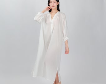 以下が含まれることがあります： ゆったりとしたシルエットの白い長袖ボタンダウンシャツドレス。Vネックとサイドスリット入りです。