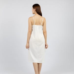 May include: A white sleeveless midi dress with a scoop neck and a simple design. The dress is made of a soft, flowing fabric.