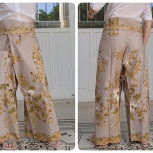 Könnte beinhalten: Eine beige Hose mit weitem Bein und einem floralen Muster in Gold- und Weißtönen. Die Hose wird mit einem Band in der Taille gebunden.