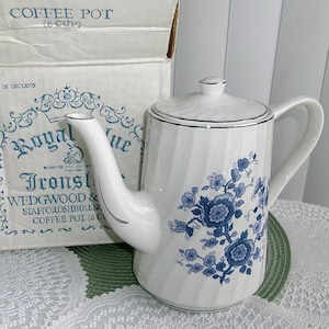 May include: White ceramic coffee pot with a blue floral design and silver trim. The pot has a lid and a handle. The box behind the pot reads "Royal Blue Ironstone" and "Coffee Pot (6 Cup)".