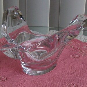 May include: A clear glass bowl with a unique, abstract design. The bowl has a wide, open mouth and a narrow base. It is made of thick, heavy glass and has a smooth, polished finish.