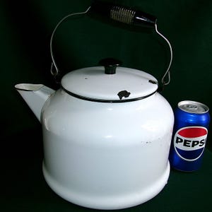May include: White enamel kettle with a black handle and lid knob. The kettle has a spout and a wire handle. A blue Pepsi can is next to the kettle. The kettle appears to be vintage.