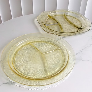 May include: Two vintage yellow glass divided serving platters. One is round with three sections, the other is a scalloped shape with two sections. Both feature an embossed floral pattern. The platters are on a white surface.