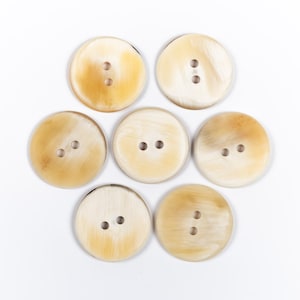 May include: Eight round, cream-colored buttons with two holes each. The buttons are made of natural horn and have a slightly textured surface.