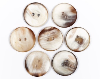 May include: Seven round, brown and white horn buttons with two holes each.