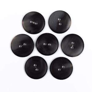 May include: Seven black horn buttons with two holes each. The buttons are arranged in a circle on a white background.