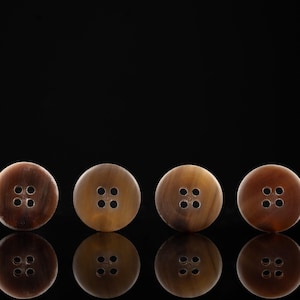 May include: Four brown and black buttons with four holes each, arranged in a row on a black background.